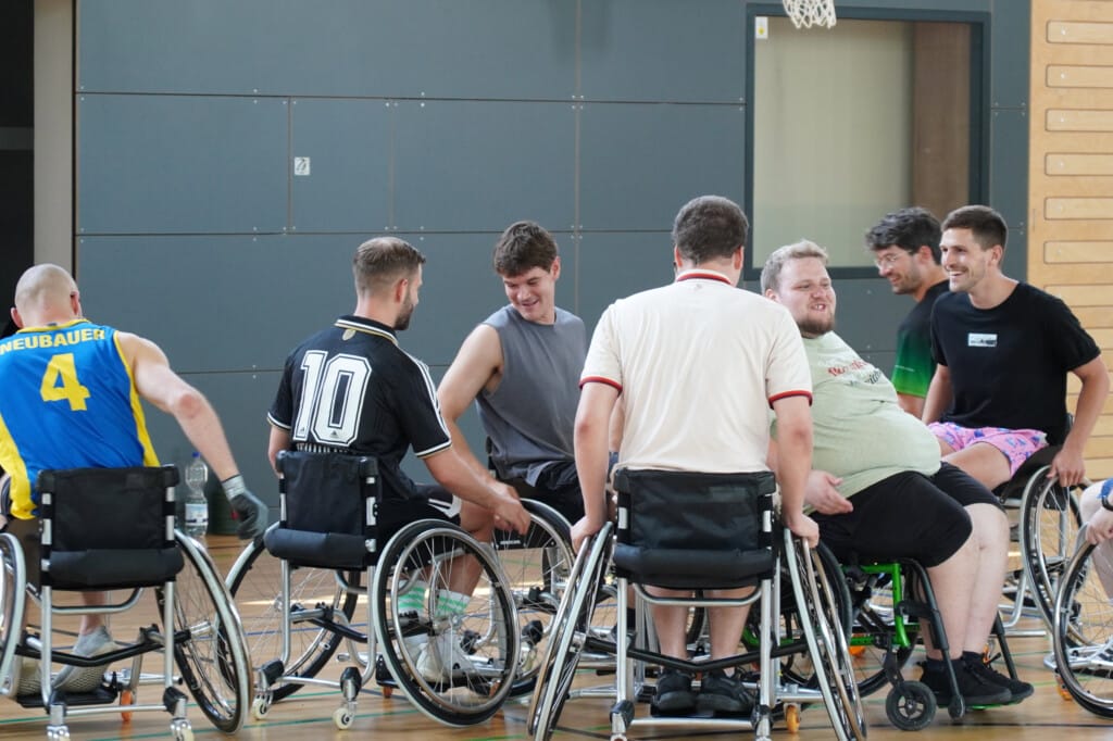Gruppe an Menschen die mit Rollstuhl durch Sporthalle fährt