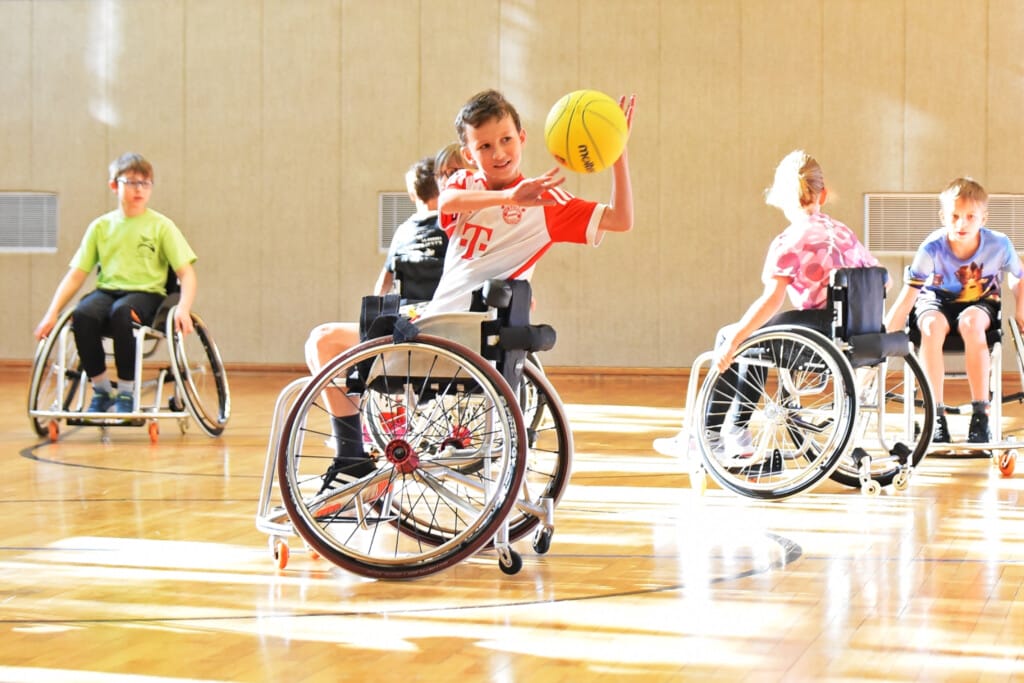 Kinder spielen Rollstuhlbasketball in Turnhalle, Kind in der Mitte wirft Ball