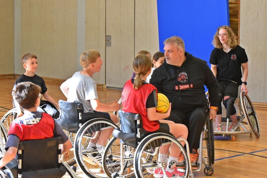 Kinder sind mit Rollstuhl in Sporthalle und reden mit RSV Bayreuth Mitgliedern