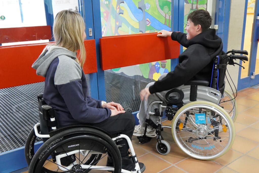zwei Schüler stehen im Rollstuhl vor Tür