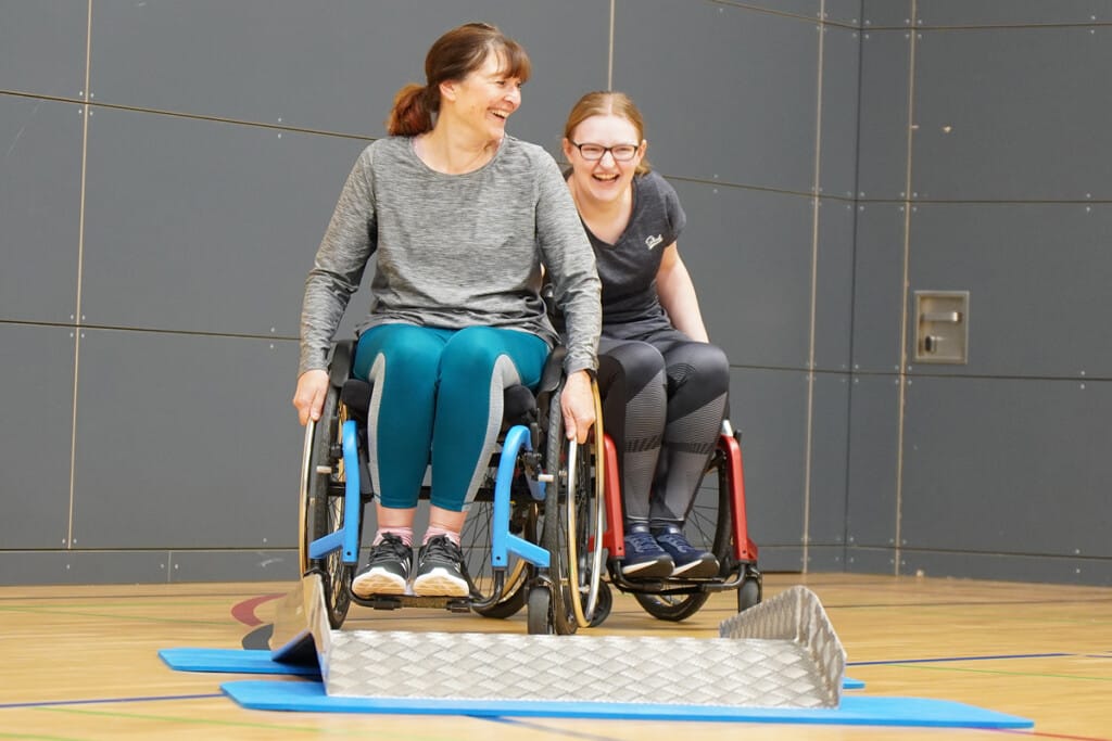 Zwei Teilnehmerinnen absolvieren bei einem Firmenevent des RSV Bayreuth gemeinsam einen Parcours im Sportrollstuhl.