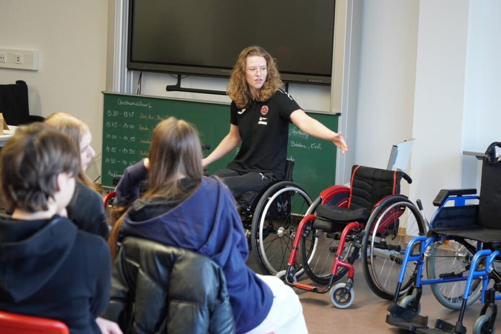 Dagmar van Hinte vom RSV Bayreuth spricht bei einem Schulprojekt mit Schülerinnen und Schülern über Rollstuhlsport.